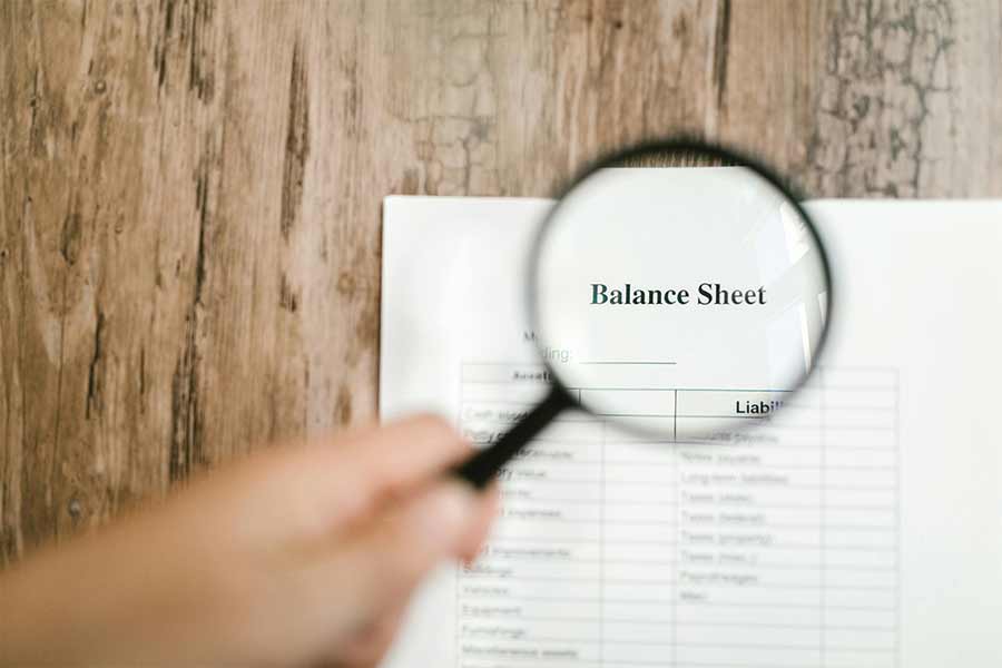 What is a balance sheet event blog image, with a magnifying glass over a balance sheet. Photo by RDNE Stock project: https://www.pexels.com/photo/a-hand-holding-a-magnifying-glass-near-wooden-table-7821689/